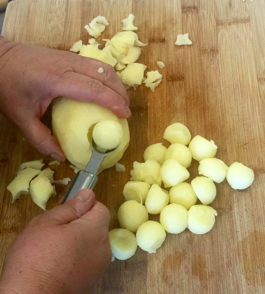 Hands shaping potato balls with a melon baller