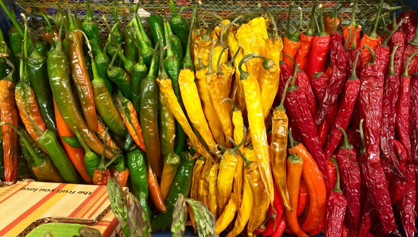 Baskets of green, yellow and red chillies at a market stall