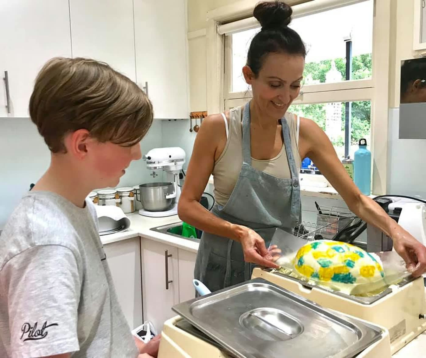 A boy watching closely as a bright yellow celebration cake is finished