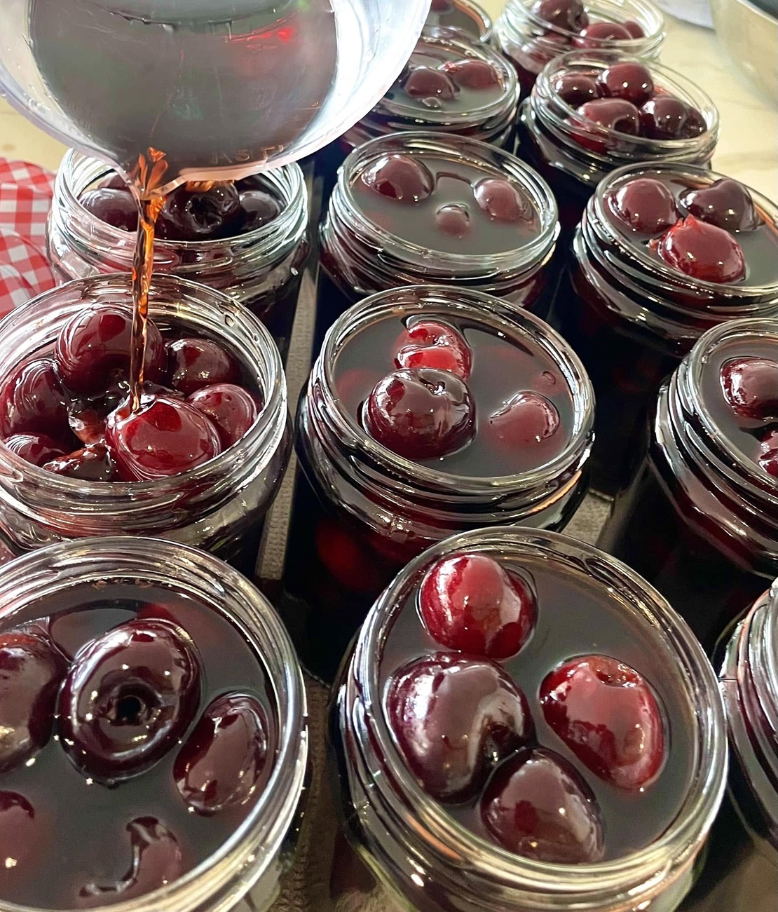 Dark syrup being poured into jars of preserved cherries