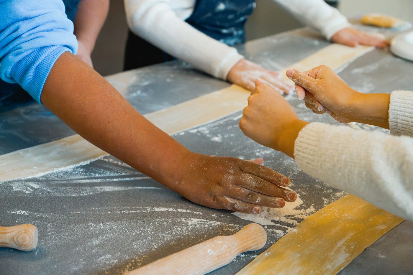 Young hands pressing and rolling strips of dough along a floured bench