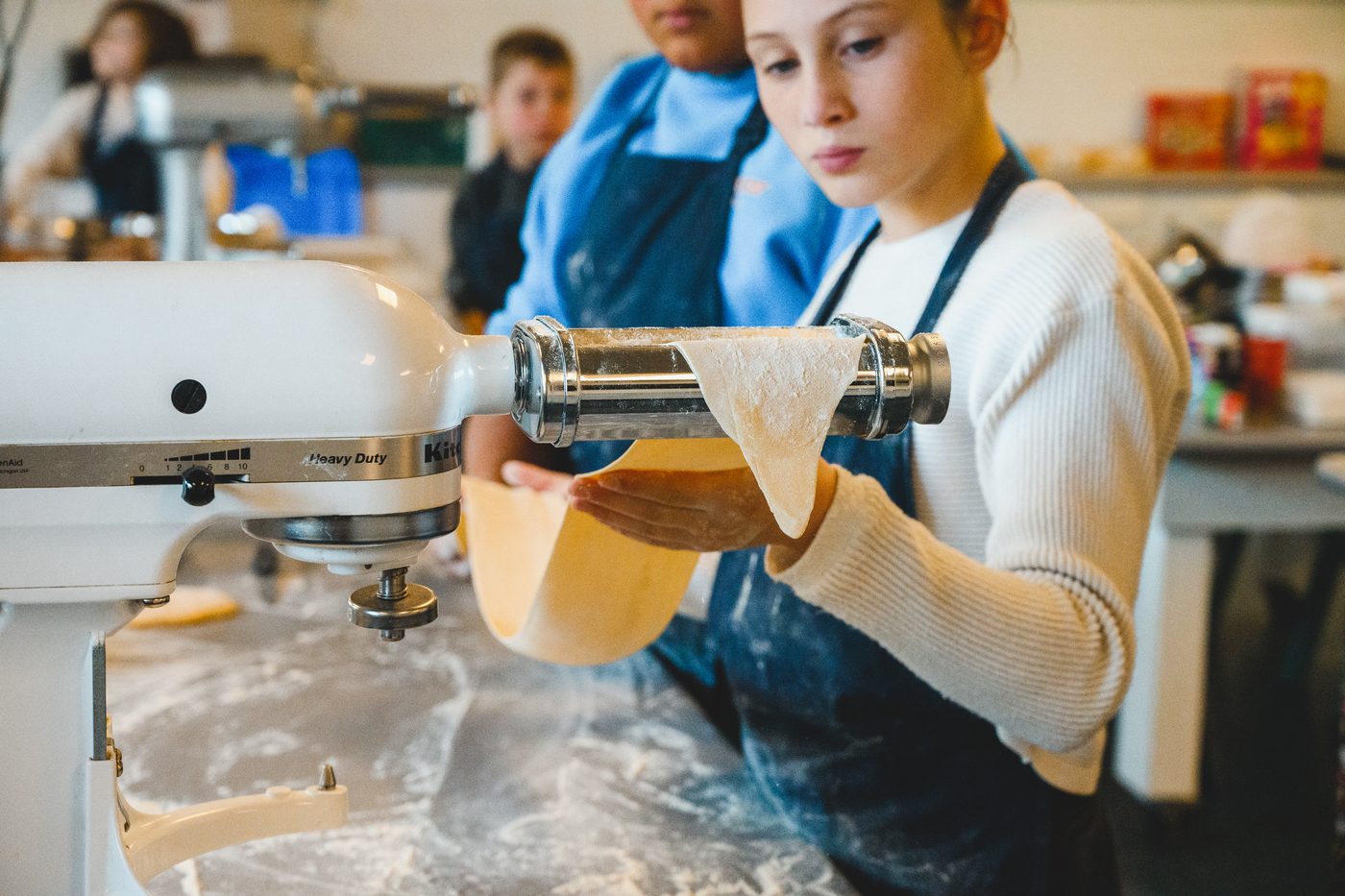 Close up of a student feeding a sheet of pasta dough through the roller