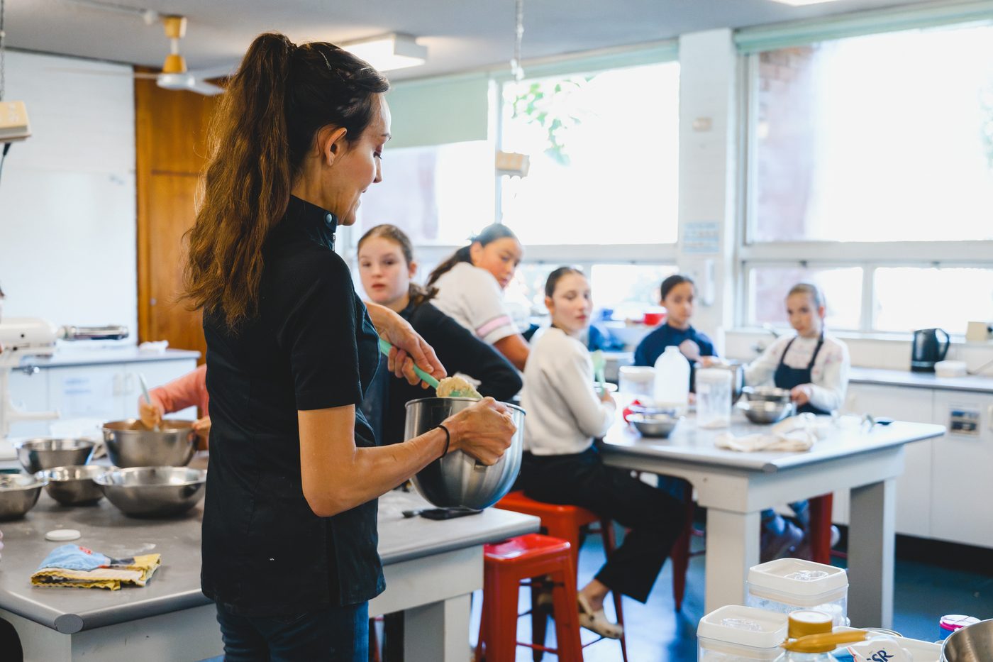Yvonne demonstrating a mix to the class, students seated around the benches