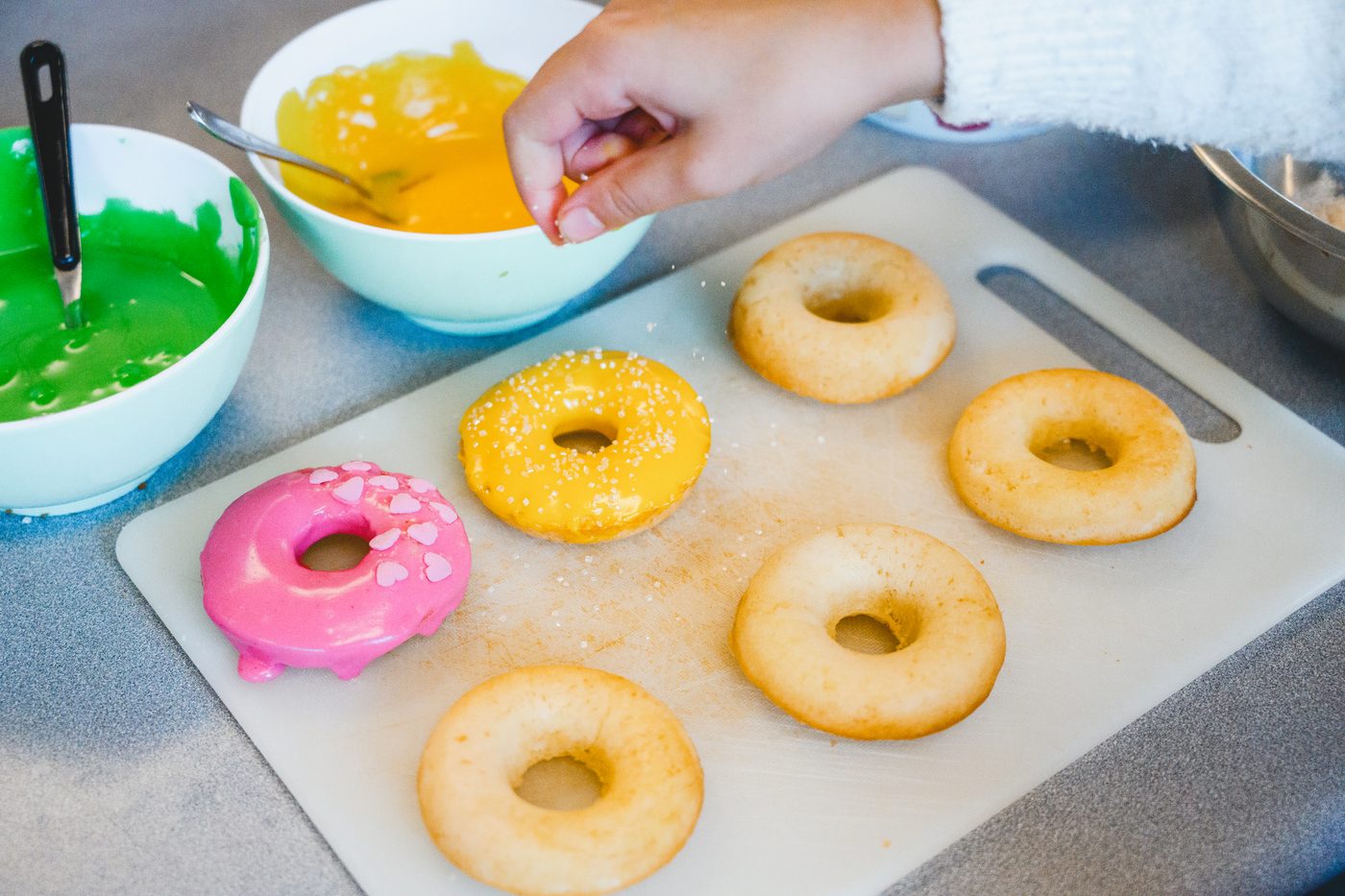 Doughnuts being iced in pink and lemon, with sprinkles going on top