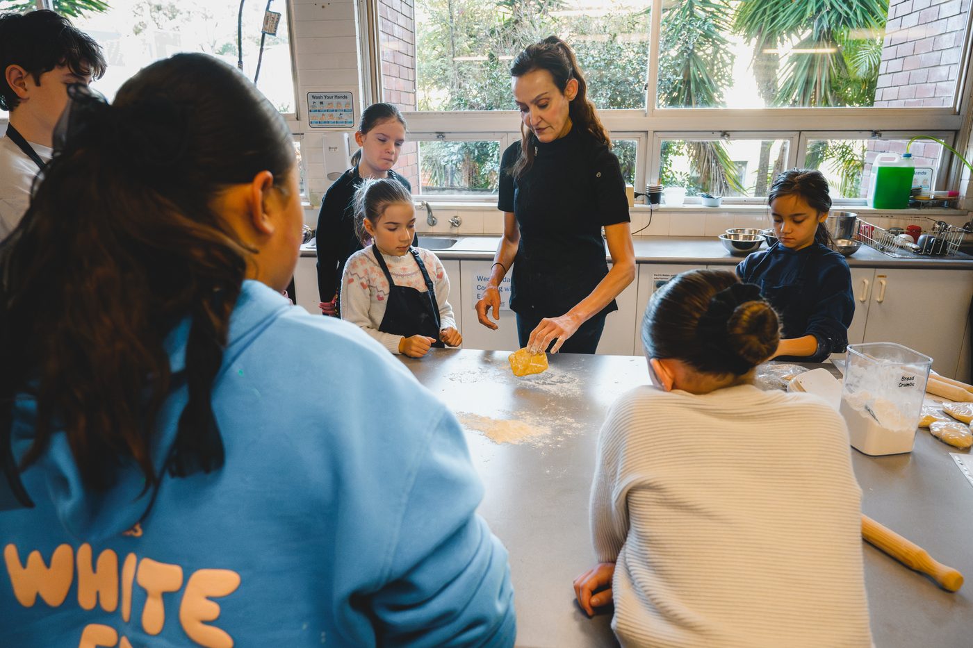 Yvonne shaping dough at the bench while a group of children watch closely