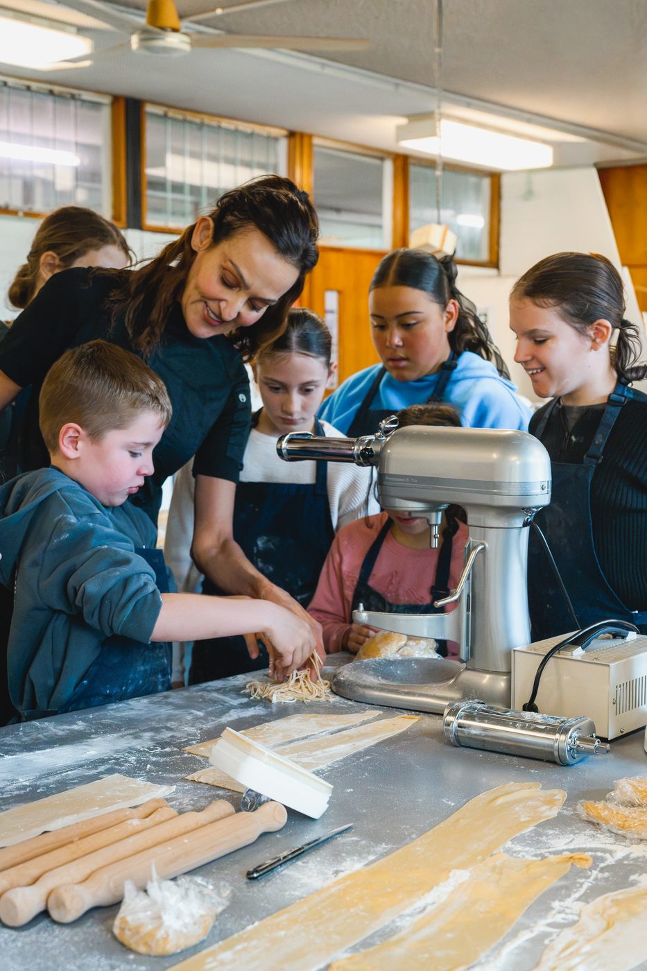 Yvonne and a group of students gathered around the pasta cutter, fresh sheets laid out ready