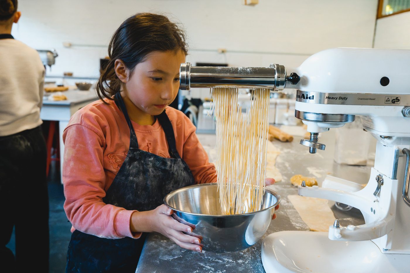 A girl catching fresh spaghetti in a bowl as it comes off the pasta cutter