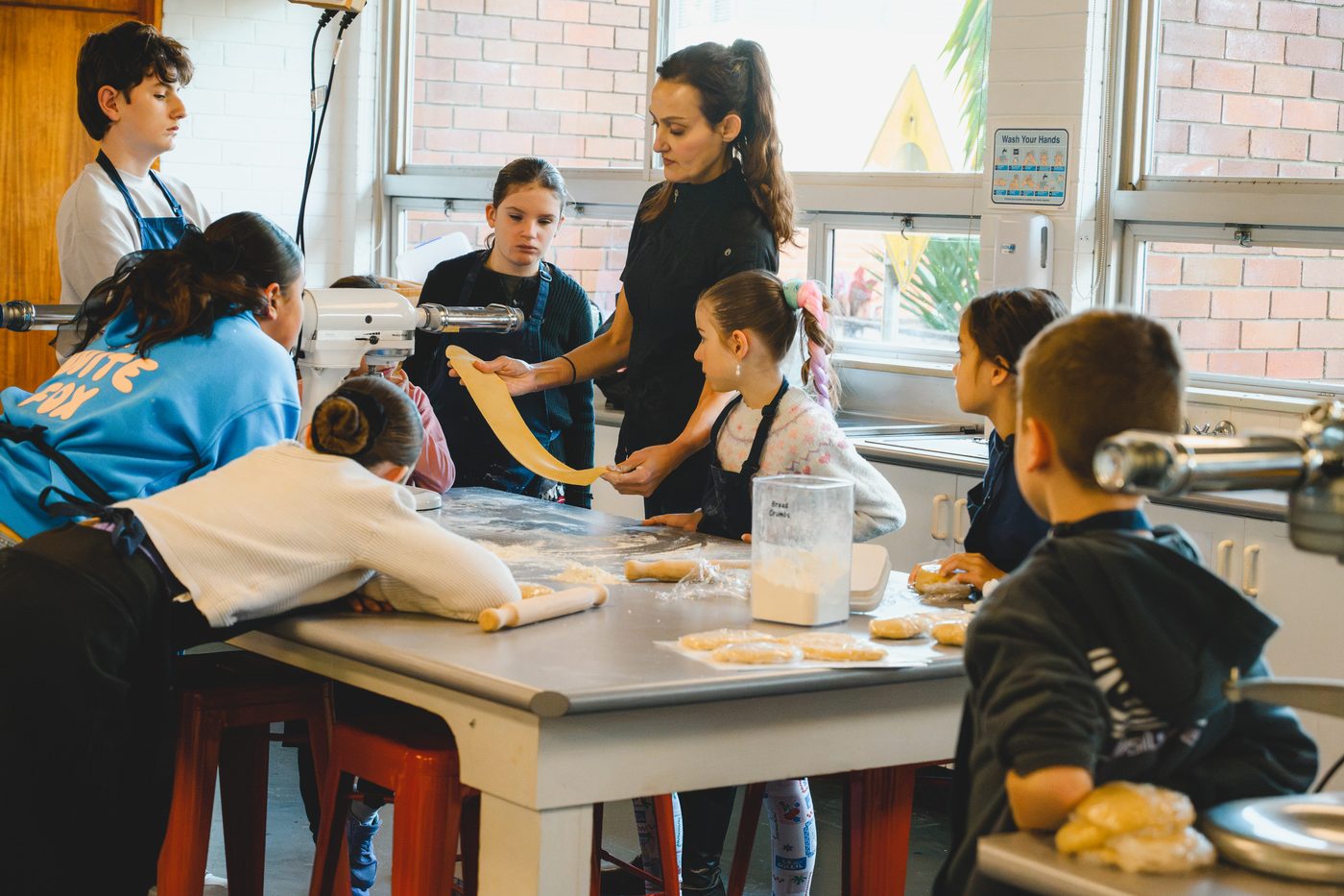 Students and helpers crowded around the bench rolling and cutting fresh pasta