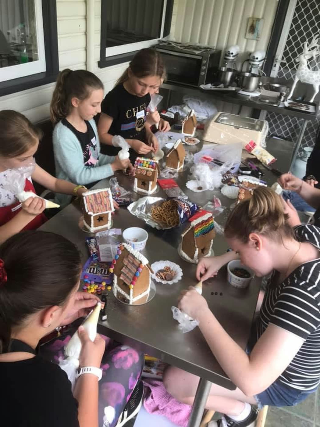 Gingerbread houses being decorated around the steel bench, piping bags in hand