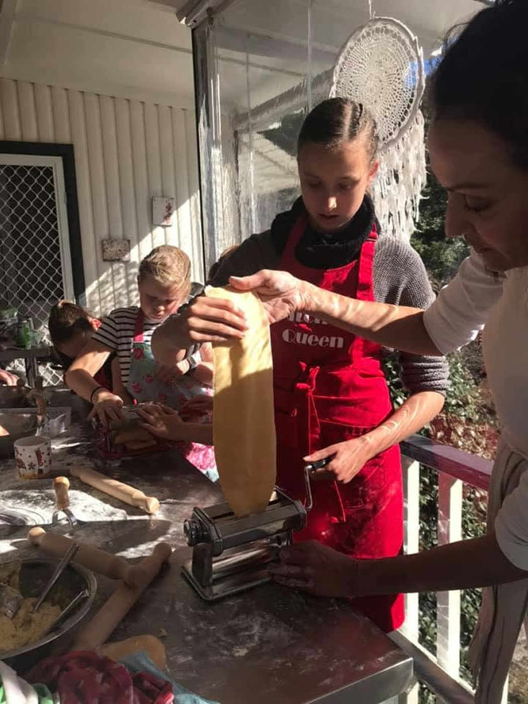 A girl feeding dough through the pasta machine while an adult guides the sheet
