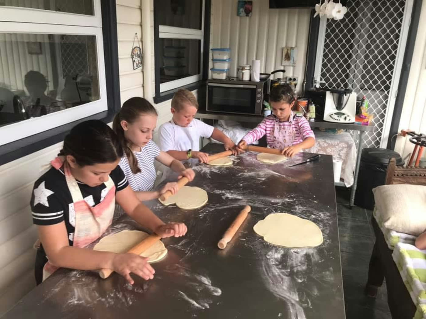 Children rolling dough out into neat circles ready for topping