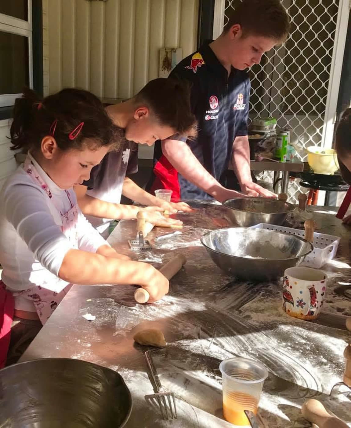 Children rolling dough along a floured kitchen bench, flour everywhere