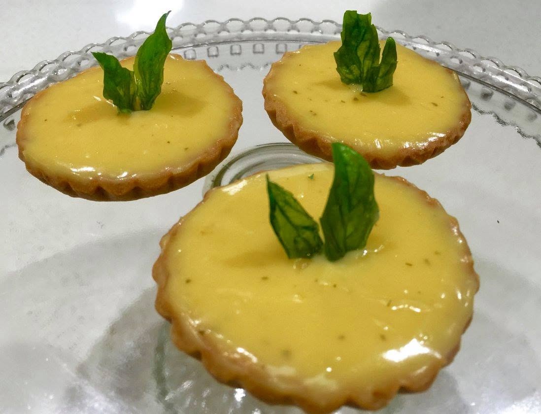 Lemon curd tartlets, each finished with a sprig of basil