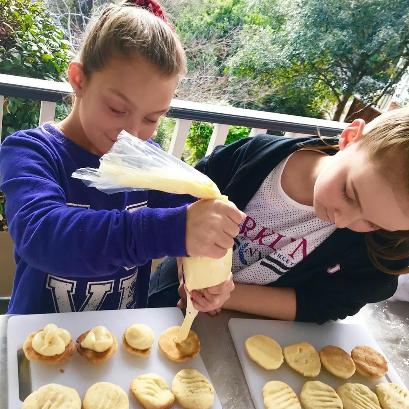 A boy piping cream onto a tray of melting moments while a friend watches closely