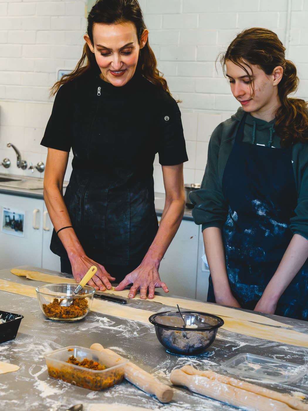 Yvonne working alongside a student at a floured bench, both shaping dough